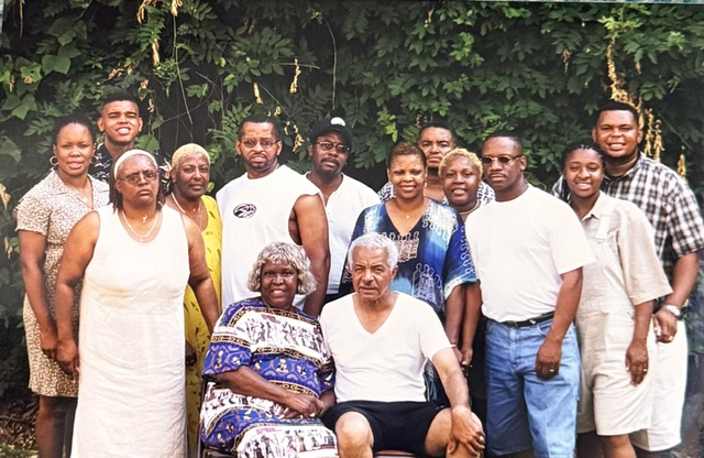 Large family group gathered in front of leafy vines